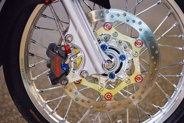 Trên bản độ này, cặp mâm đúc nguyên bản của Exciter 135 đã được chủ xe thay bằng niềng nhôm Excel nhẹ và sắc sảo hơn. Điểm nhấn thực sự ở "dàn chân" trước của xe nằm ở hệ thống phanh khá "khủng" với heo Brembo Billet 2 piston đối xứng kèm pad nhôm CNC và đĩa Brembo full-floating.