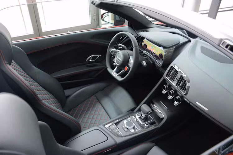 Các chi tiết thiết kế còn lại của R8 Spyder, bao gồm cả nội thất hoàn toàn giống như R8 Coupe. Xe có bảng điều khiển tối giản, bảng đồng hồ kỹ thuật số Virtual Cockpit và những chiếc ghế bọc da chần chỉ vân con thoi sang trọng. Đương nhiên, với bộ mui xếp mới, R8 Spyder sẽ có thêm một nút bấm đóng mở mui trên bệ điều khiển trung tâm ốp sợi carbon.