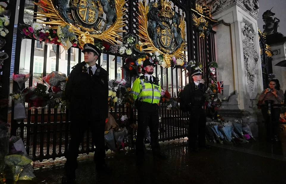 Người dân đặt những bó hoa tươi ở cổng cung điện Buckingham trong khi cảnh sát đứng canh gác.