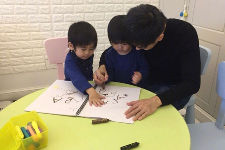 Hình ảnh Lâm Chí Dĩnh hướng dẫn con trai tập viết chữ cái tiếng Anh.