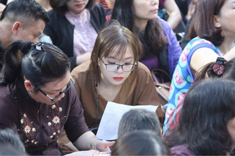 Một cô gái trẻ cầm tờ kinh đã được in sẵn, ngồi trong sân chùa Phúc Khánh tham gia làm lễ.