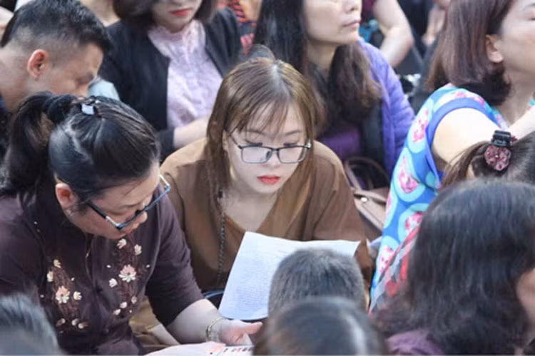 Một cô gái trẻ cầm tờ kinh đã được in sẵn, ngồi trong sân chùa Phúc Khánh tham gia làm lễ.