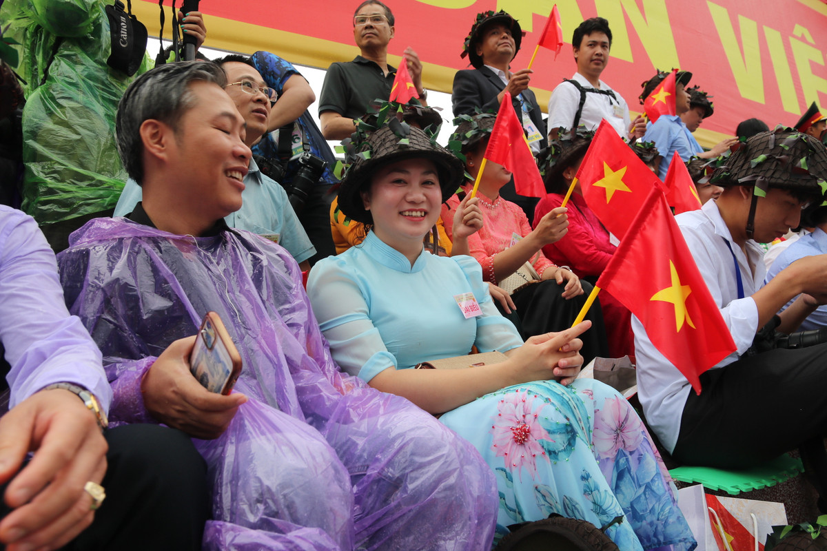 Khoảng 6h50, trời bỗng dưng đổ mưa lớn. Người dân đứng xem đại lễ trong cơn mưa với nụ cười như "tỏa nắng", xua đi cái âm u của thời tiết không thuận lợi.