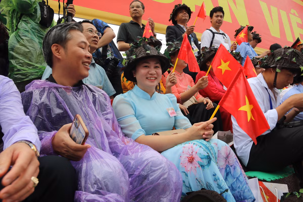 Khoảng 6h50, trời bỗng dưng đổ mưa lớn. Người dân đứng xem đại lễ trong cơn mưa với nụ cười như "tỏa nắng", xua đi cái âm u của thời tiết không thuận lợi.