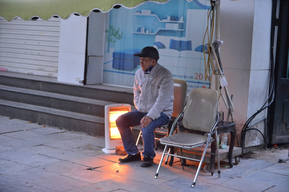 Một người dân vừa trông cửa hàng ngồi bên cạnh máy sưởi. (Ảnh: Saostar) 