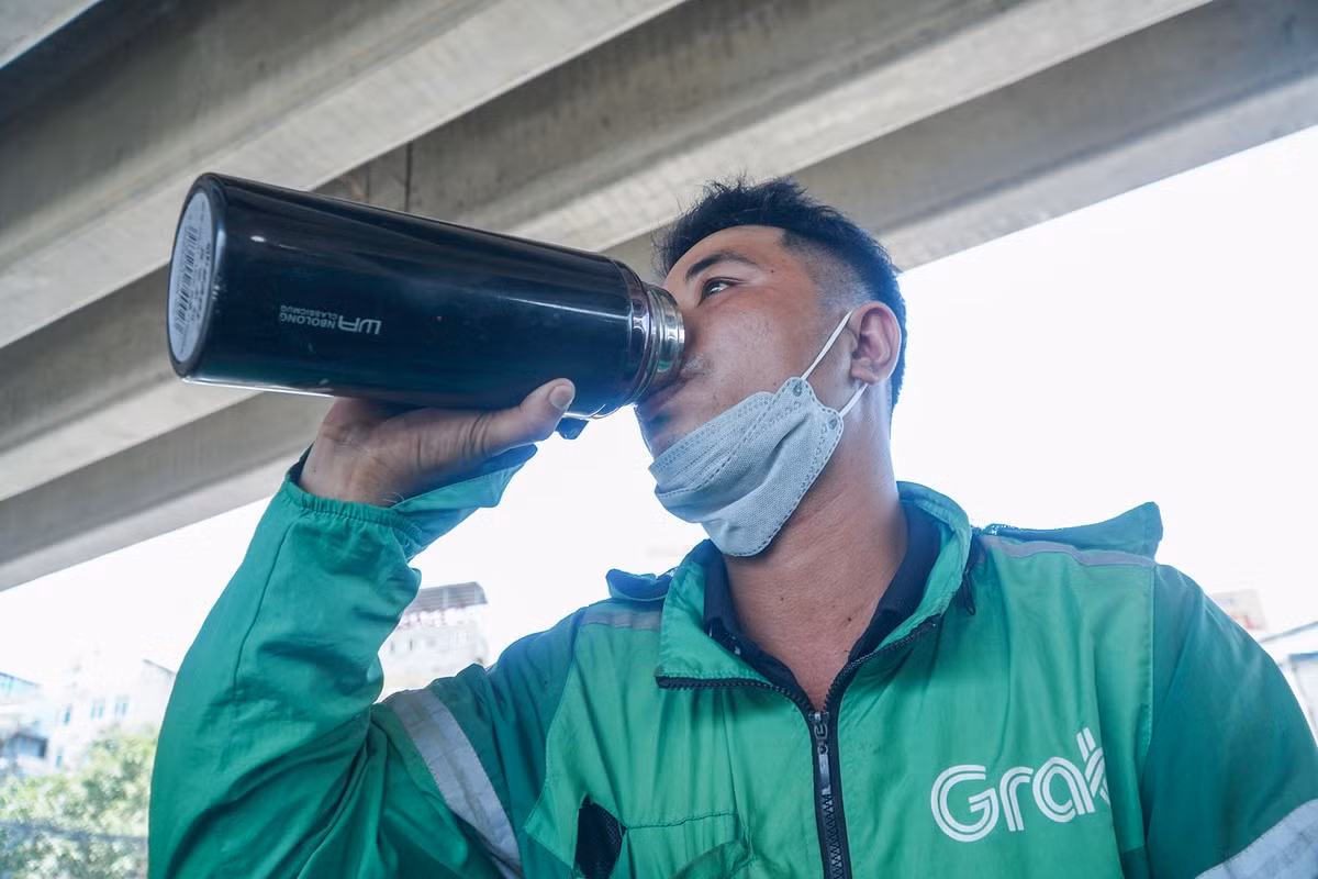 Cạnh đó, một tài xế xe ôm công nghệ vừa hoàn thành việc trả khách, tranh thủ đỗ vào gầm cầu để uống nước lấy lại sức khỏe giữa thời tiết oi bức. Người lao động tự do thường tận dụng gầm cầu, bóng cây là nơi nghỉ ngơi sau những giờ làm việc vất vả.