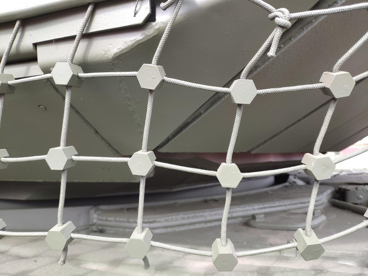 Đặc biệt, bên dưới kẽ hở của tháp pháo là nơi hiểm yếu của xe, được trang bị hệ thống giáp lưới để đánh chặn các loại đầu đạn chống tăng của đối phương. Nó sử dụng kết cấu lưới kết hợp với các nút kim loại, giúp chống lại đạn súng chống tăng RPG hiệu quả, nâng cao khả năng bảo vệ của xe lên rất nhiều. Ảnh: Cận cảnh hệ thống giáp lưới trên xe tăng T-90M