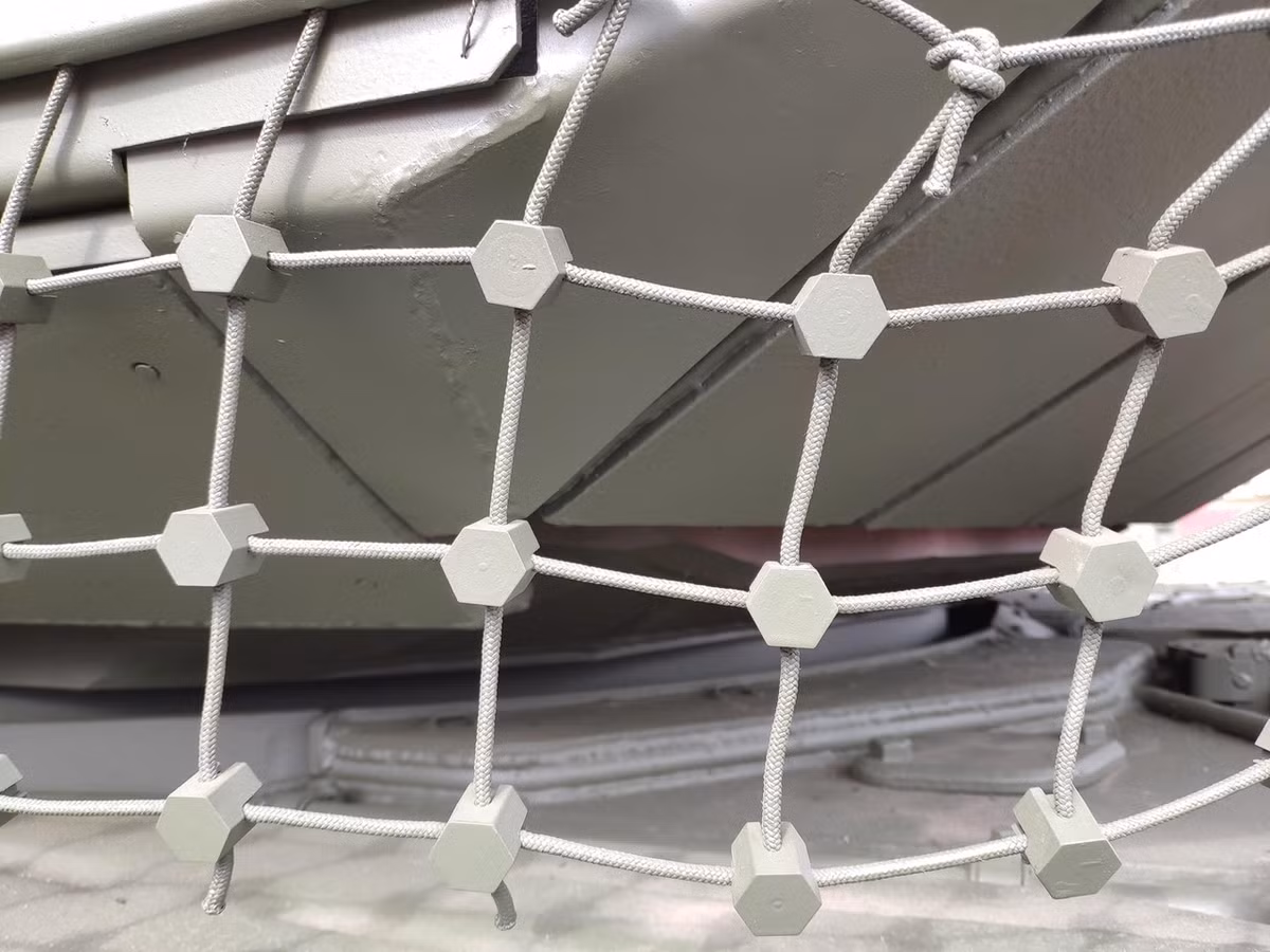 Đặc biệt, bên dưới kẽ hở của tháp pháo là nơi hiểm yếu của xe, được trang bị hệ thống giáp lưới để đánh chặn các loại đầu đạn chống tăng của đối phương. Nó sử dụng kết cấu lưới kết hợp với các nút kim loại, giúp chống lại đạn súng chống tăng RPG hiệu quả, nâng cao khả năng bảo vệ của xe lên rất nhiều. Ảnh: Cận cảnh hệ thống giáp lưới trên xe tăng T-90M