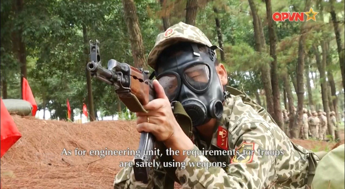 Không những vậy, giữa cái nắng oi ả trên thao trường, người chiến sĩ còn phải thực hiện huấn luyện tác chiến khi đeo mặt nạ phòng hóa để làm quen với trường hợp địch sử dụng vũ khí hóa học. Việc sử dụng mặt nạ làm giảm đáng kể tầm quan sát của chiến sĩ cùng với đó là hạn chế quá trình hô hấp tuy nhiên lại là khoa mục vô cùng sát thực tế chiến đấu trên chiến trường, đòi hỏi người lính phải có sức khỏe tốt và quen thuộc với điều kiện chiến đấu. Ảnh: Chiến sĩ đặc công huấn luyện bắn AK khi đeo mặt nạ phòng hóa.
