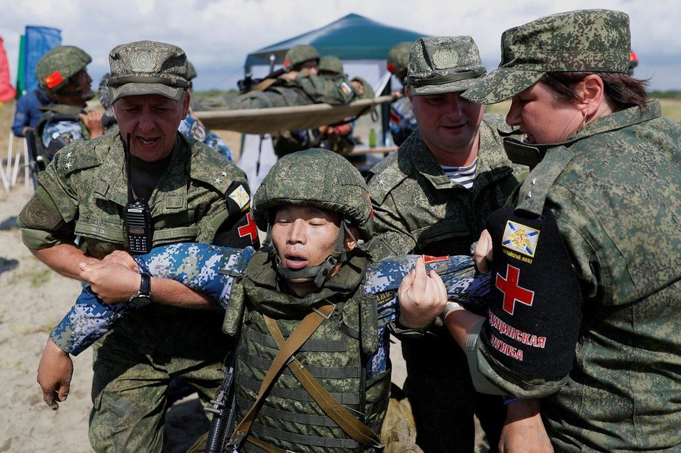 Do sự hoành hành của COVID-19 tại nhiều quốc gia trên thế giới, để đảm bảo an toàn, Bộ quốc phòng Nga đã tổ chức một số cuộc họp để hoàn thiện và công bố lịch trình như sau: Từ ngày 4 - 10/8 tới đây, nước tổ chức sẽ nhận các đội thi và kiểm tra sức khỏe nhằm phát hiện sớm virus nếu có và thực hiện biện pháp cách ly. Từ ngày 10 - 22/8, tiếp quản và phân phát vũ khí tiêu chuẩn theo thể lệ cuộc thi cho các đội thi nhằm huấn luyện trước với khí tài. Ảnh: Một binh sĩ Trung Quốc đang được dìu bởi các Quân y thuộc Hải quân Nga trong một phần thi của ARMY Games.