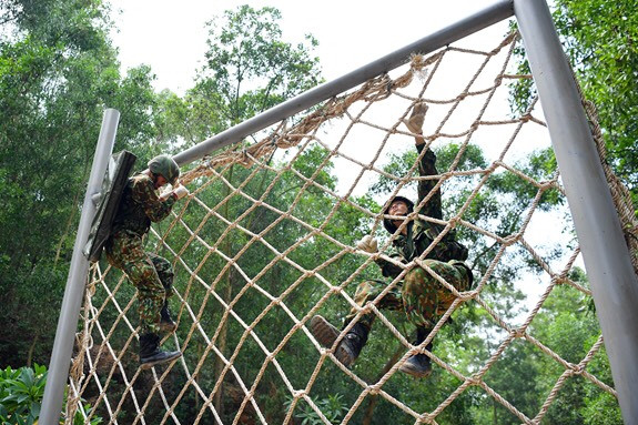 Ngoài ra, chiến sĩ phải mang áo giáp và mũ chống đạn chuẩn do nước chủ nhà cung cấp, mang súng tiểu liên AK và bộ thiết bị rà phá vật nổ. Dù vẫn còn thiết thốn về trang thiết bị, tuy nhiên Các cấp lãnh đạo vẫn tạo điều kiện tốt nhất cho cán bộ chiến sĩ có được những trang bị sát thực tiễn bài thi, đảm bảo cho vận động viên cảm giác tốt nhất. Ảnh: Chiến sĩ công binh thực hiện nội dung vượt tường lưới - Nguồn: QĐND