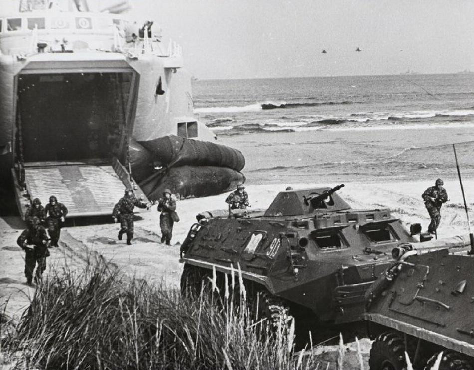 Sau khi cơ động ủi bãi lao lên bờ, khoang tàu đệm khí sẽ mở ra cho xe thiết giáp và xe tăng phối thuộc cùng với chiến sĩ hải quân đánh bộ nhanh chóng tiến lên bờ. Trước đó, các loại hỏa lực từ tàu như pháo phản lực, pháo hạm cùng rocket từ máy bay trực thăng vũ trang đồng loạt khai hỏa nhằm dọn bãi đổ bộ và triệt hạ sức đề kháng của đối phương phòng thủ trên bờ, tạo điều kiện cho quân ta chiếm lĩnh trận địa dễ dàng. Ảnh: Xe thiết giáp BTR-60PB tiến lên bờ phối thuộc với binh sĩ từ tàu đổ bộ.