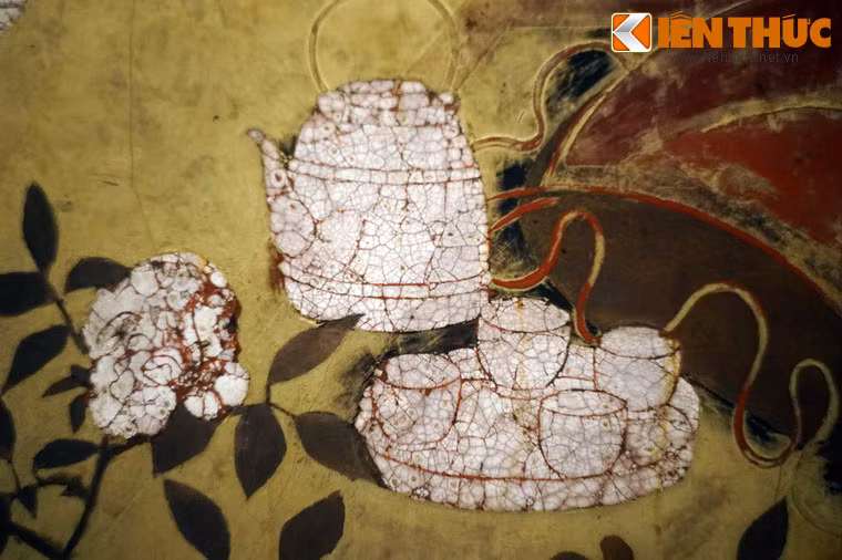 Bên một người phụ nữ có bình trà và bộ chén bốn chiếc đặt trên khay.