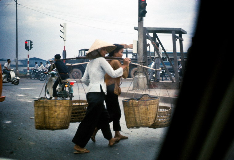 Những người phụ nữ với đôi quang gánh di chuyển trên xa lộ.