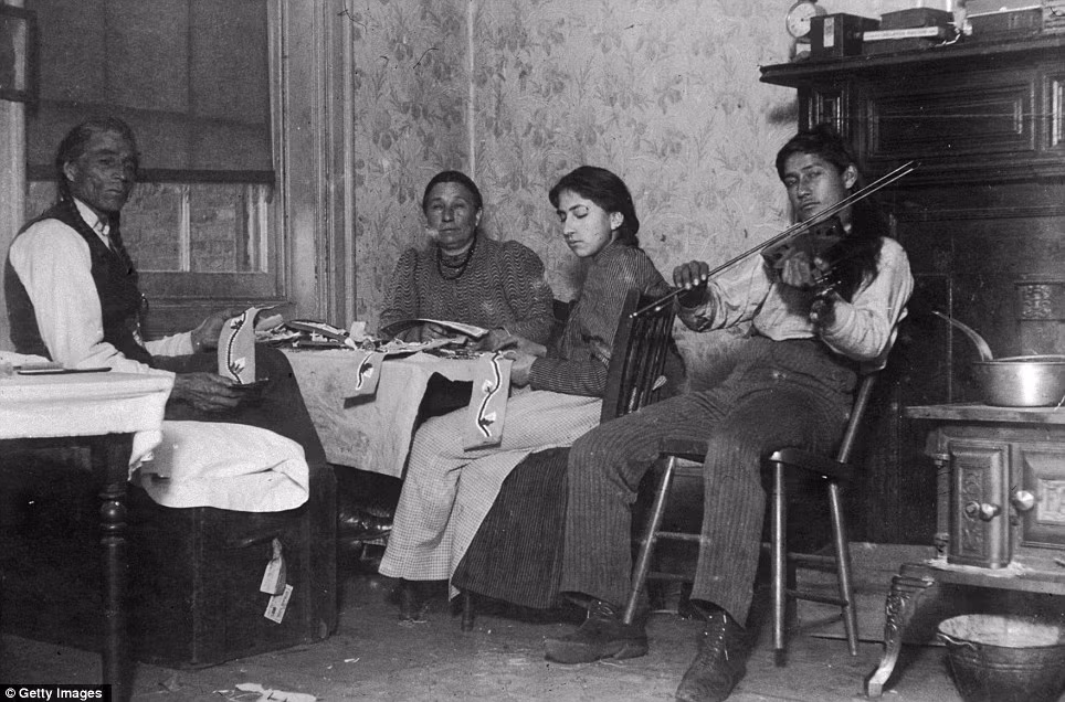 Hai vợ chồng cùng con gái làm đồ thủ công mỹ nghệ trong khi người con trai say sưa chơi violin tại ngôi nhà của họ nằm tại số 6 phố Beach, New York năm 1895.