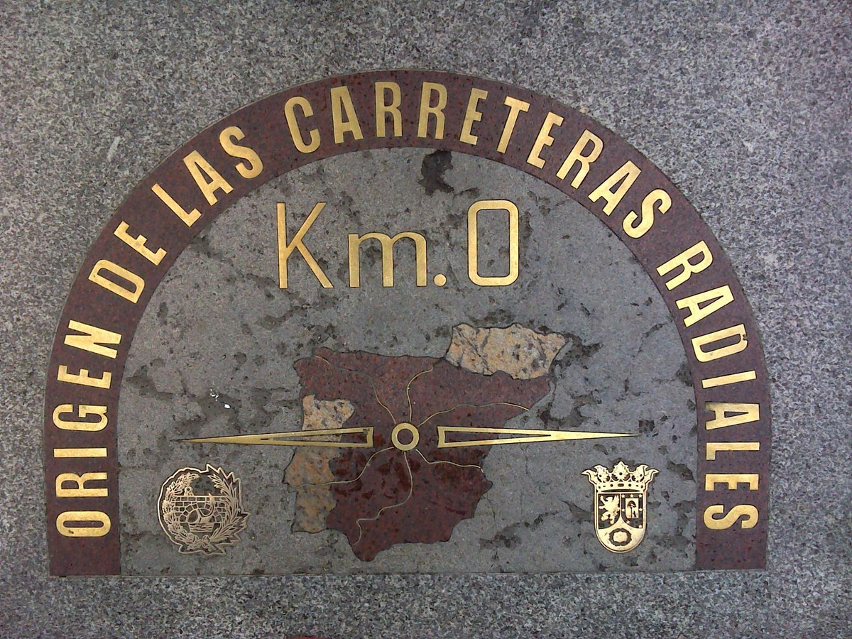 Km0 của Tây Ban Nha nằm ở trung tâm quảng trường Puerta del Sol, thủ đô Madrid. Puerta del Sol trước đây là cổng thành bao quanh Madrid nhưng nay là điểm kết nối của nhiều con phố cổ. Gần cột mốc số 0 còn có tòa Nhà bưu điện Hoàng gia - nơi có chiếc đồng hồ nổi tiếng thế giới sẽ vang lên những tiếng chuông khi giao thừa, báo hiệu năm mới đã đến.