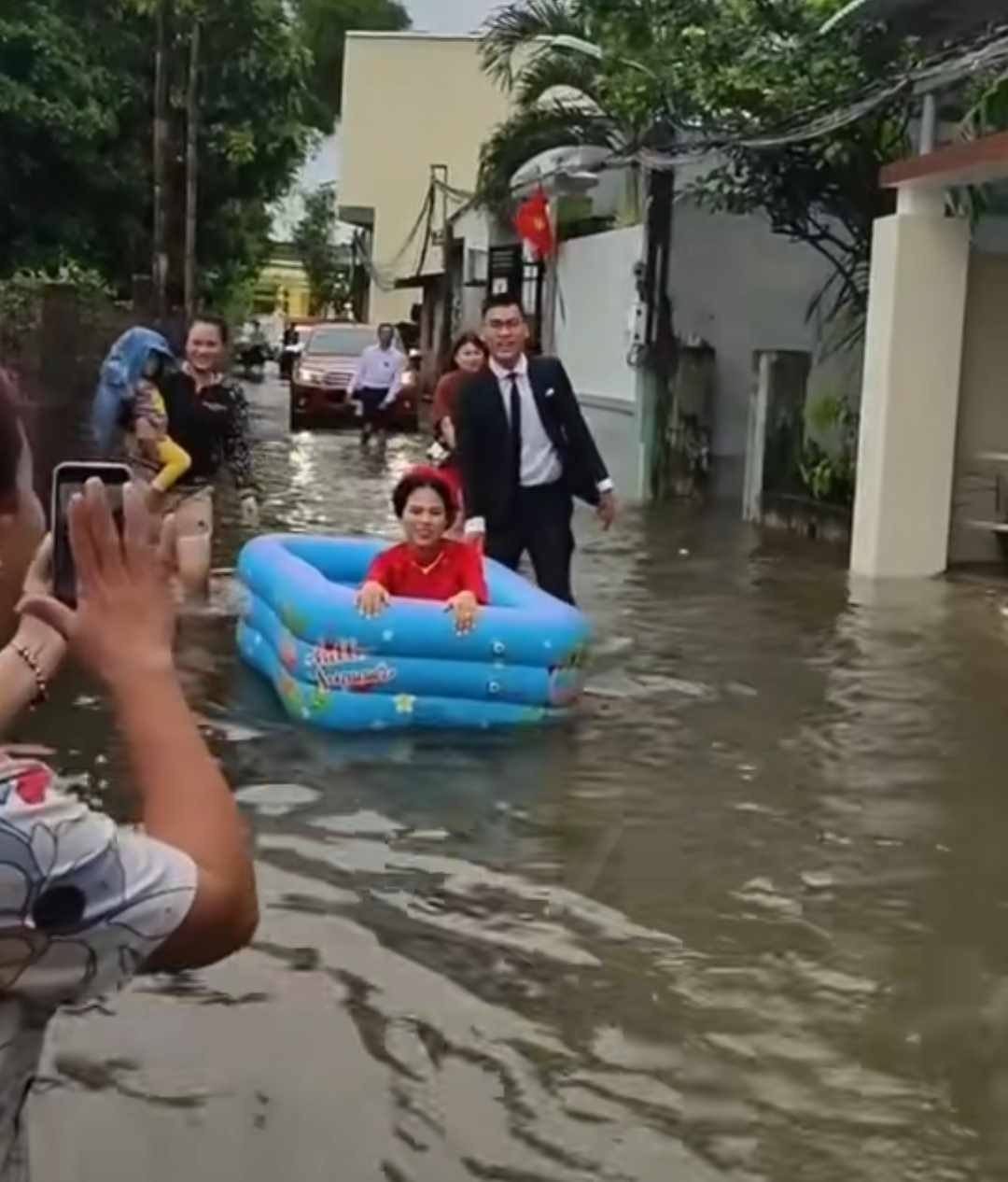 Theo hình ảnh chia sẻ, để dễ dàng di chuyển, cô dâu đã sử dụng phao bơi trẻ em làm phương tiện, bên cạnh là chú rể dùng tay đẩy đi qua đoạn đường ngập nước lũ một cách nhẹ nhàng.