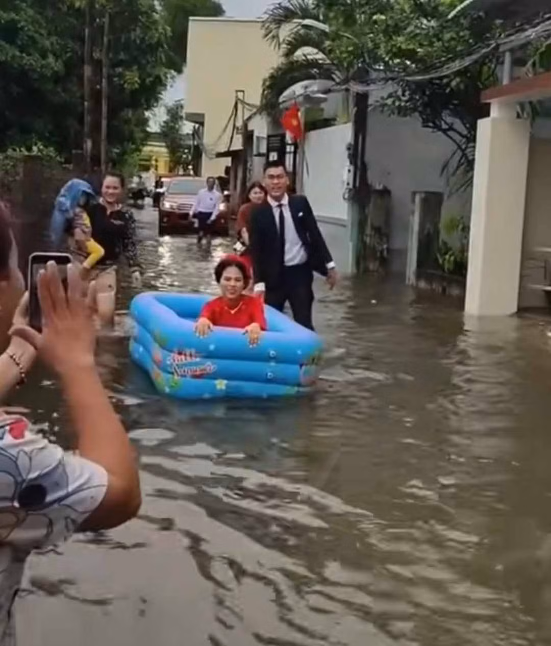 Theo hình ảnh chia sẻ, để dễ dàng di chuyển, cô dâu đã sử dụng phao bơi trẻ em làm phương tiện, bên cạnh là chú rể dùng tay đẩy đi qua đoạn đường ngập nước lũ một cách nhẹ nhàng.