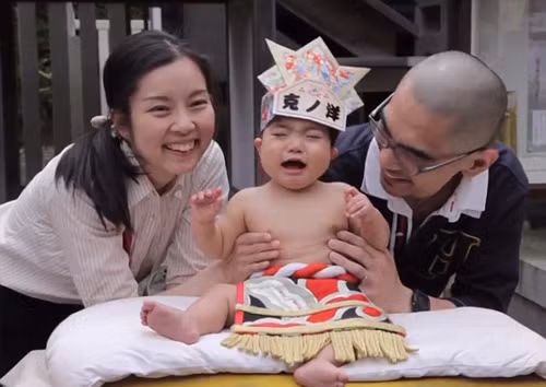 Trong ảnh là một cậu nhóc vừa bị trêu khóc rất to bởi các võ sĩ sumo, trong khi đó, bố mẹ cậu bé rất vui vẻ vì họ nghĩ rằng con mình đã thành công nhận được may mắn. (Nguồn Sina)