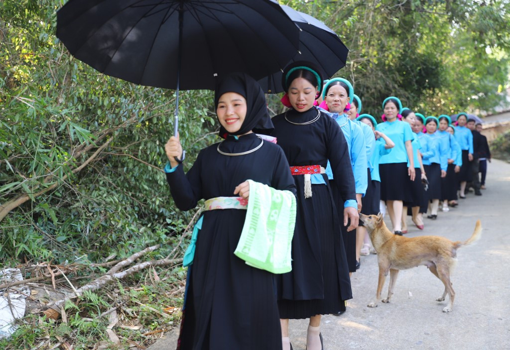 Cô dâu mặc áo dài, thắt lưng hoa, trên tay cầm chiếc khăn mặt đã được chuẩn bị sẵn; đầu đội khăn màu đen. Các cô gái khác mặc áo màu xanh đặc trưng của người Sán Chỉ. Đoàn rước dâu ra ngoài đường, việc hò hát vẫn tiếp tục.