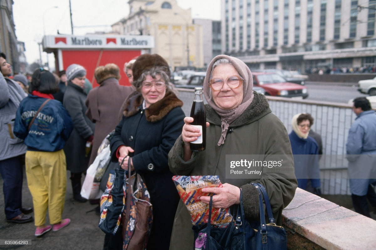 Cụ bà khoe chai Cola trên đường phố Moscow, ảnh chụp năm 1993. Phía xa là quầy thuốc lá Marlboro, một thương hiệu đến từ phương Tây.