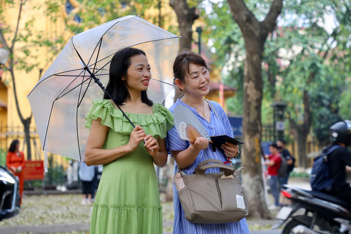 Một du khách Nhật Bản chụp ảnh kỉ niệm cùng người Việt trên con đường đẹp nhất Hà Nội phủ kín lá rụng.