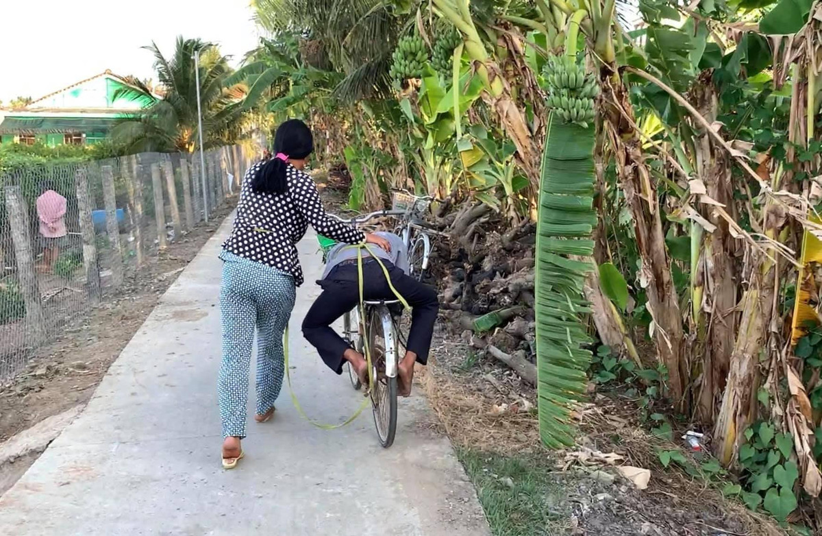 Chồng không đứng vững nổi, nên cô vợ phải lấy dây cột lại, để nằm lên yên xe rồi một tay ôm người, một tay dắt xe đi.
