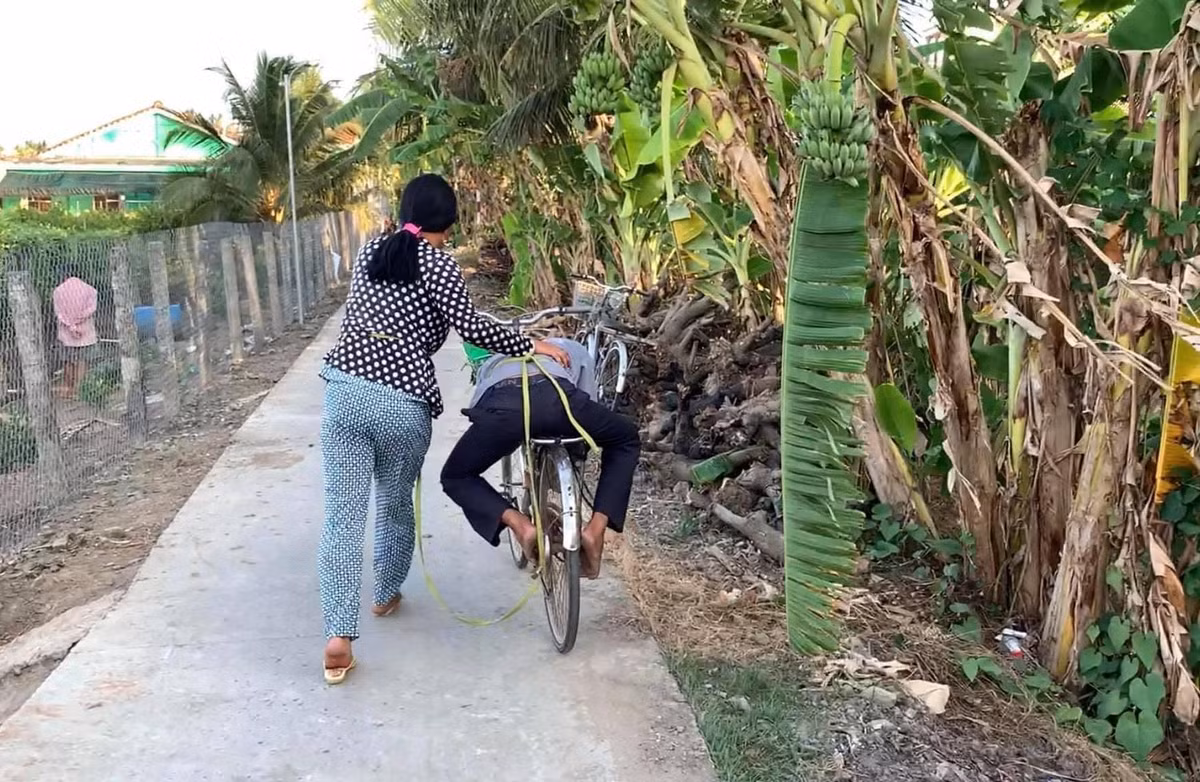 Chồng không đứng vững nổi, nên cô vợ phải lấy dây cột lại, để nằm lên yên xe rồi một tay ôm người, một tay dắt xe đi.
