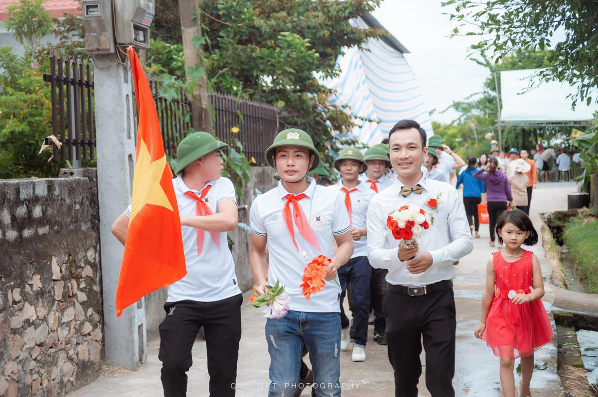 Theo hình ảnh ghi lại, thay vì diện trang phục bảnh bao như thường lệ thì dàn khách mời nhà trai lại diện đồng phục mũ cối, quàng khăn đỏ và người dẫn đoàn còn cầm theo cờ Tổ quốc.