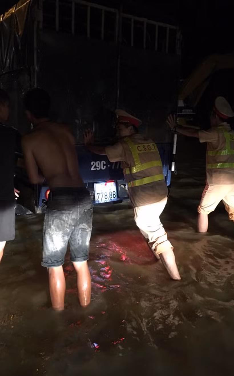 Cảnh sát cùng người dân đẩy xe vượt qua nước lũ trên đường Hồ Chí Minh.