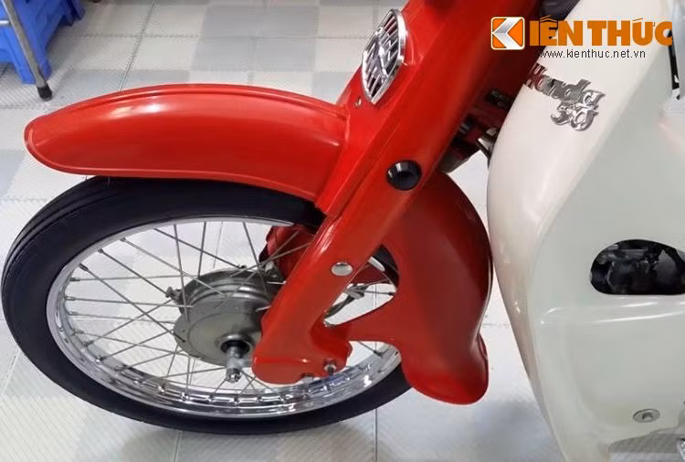 Ở phía trước, toàn bộ dè trước và giảm xóc "giò gà" đặc trưng của dòng xe Super Cub vẫn còn giữ nguyên màu sơn đỏ nguyên bản bóng lộn, không tì vết. Ngay cả các chi tiết kim loại bóng hay mạ chrome như vành hoặc moay-ơ cũng còn như mới.