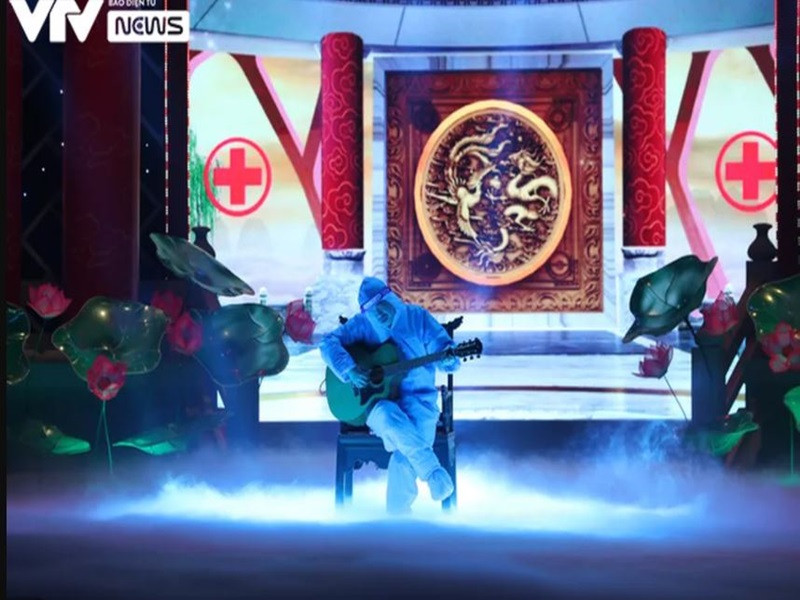 Trong một phân cảnh, "Ngọc Hoàng" Quốc Khánh mặc áo bảo hộ kín mít, ngồi đánh đàn. Ảnh: VTV
