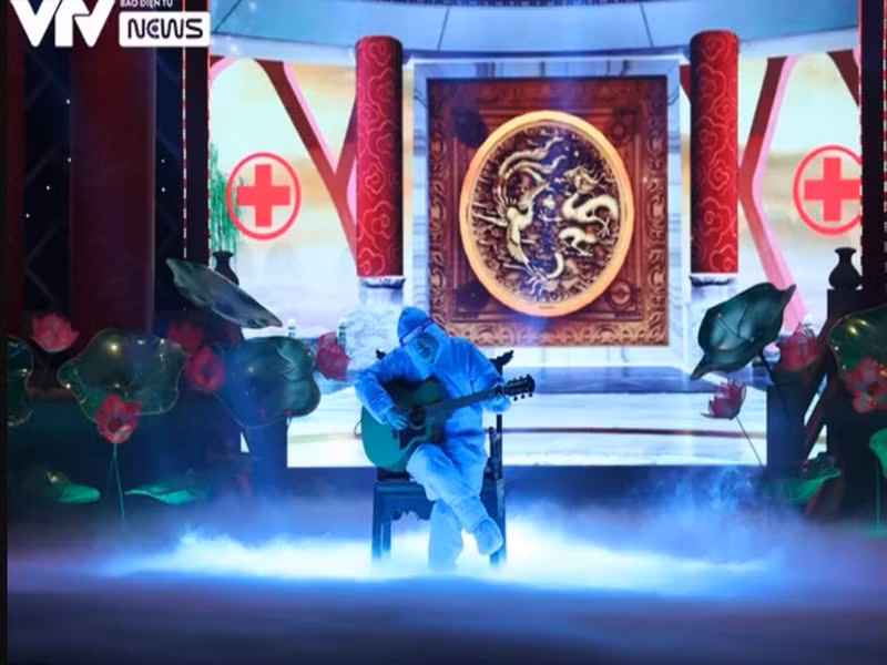 Trong một phân cảnh, "Ngọc Hoàng" Quốc Khánh mặc áo bảo hộ kín mít, ngồi đánh đàn. Ảnh: VTV
