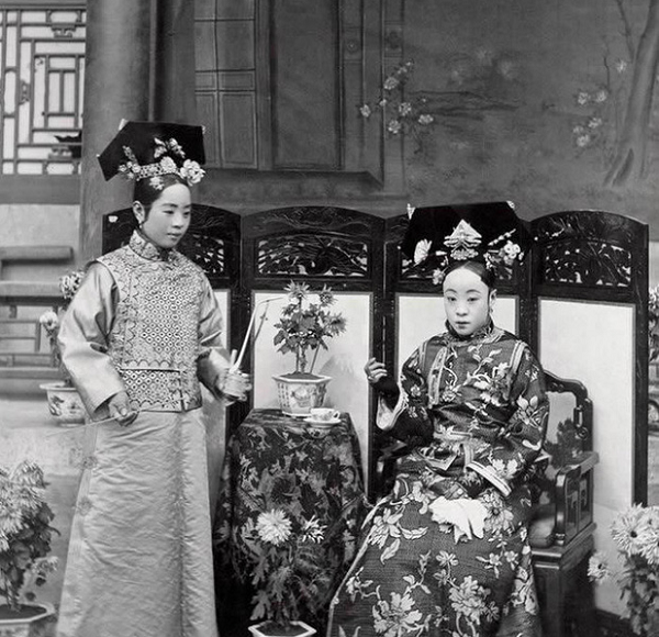 Người đang ngồi là mẹ ruột của Hoàng đế Phổ Nghi, vị Hoàng đế cuối cùng của nhà Thanh và cũng là Hoàng đế cuối cùng của chế độ phong kiến Trung Hoa. Cô gái bên trái là gia nhân của bà, đang hầu hạ bà uống trà.
