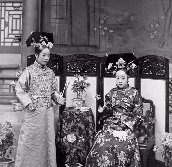 Người đang ngồi là mẹ ruột của Hoàng đế Phổ Nghi, vị Hoàng đế cuối cùng của nhà Thanh và cũng là Hoàng đế cuối cùng của chế độ phong kiến Trung Hoa. Cô gái bên trái là gia nhân của bà, đang hầu hạ bà uống trà.