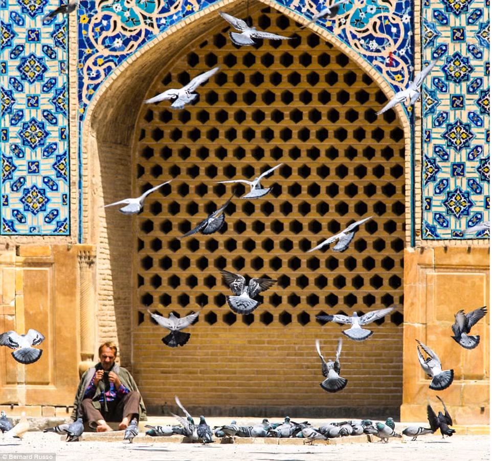 Người đàn ông ngồi trên vỉa hè giữa bầy chim bồ câu ở Kashan.