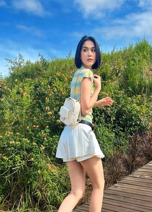 Ngọc Trinh diện chân váy ngắn xếp ly kết hợp áo phông. Cô đeo balo, đi dép sandal.