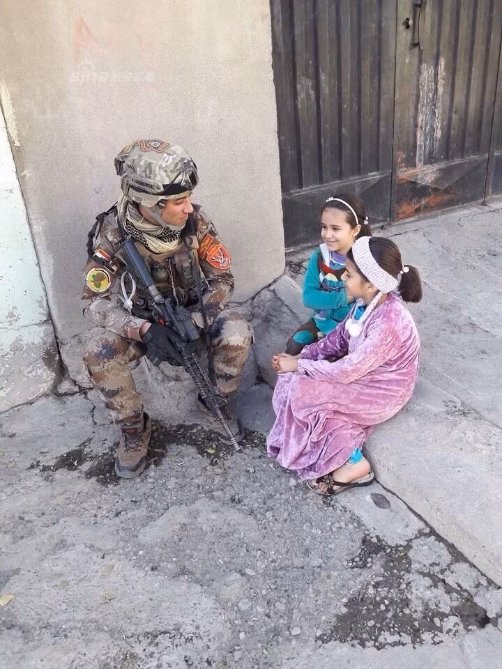 Một tay súng Quân đội Iraq đang nói chuyện với các em nhỏ ở ngoại vi Mosul. Một số vùng dân cư ở Mosul đã được giải phóng hoàn toàn sau những năm tháng khó khăn.