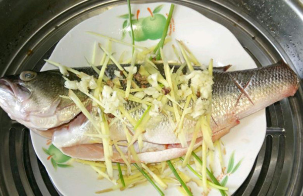 Xếp hành lá, sả và gừng lên đĩa rồi đặt cá lên trên. Tiếp tục rải một lớp hành, ớt và gừng lên phần trên thân cá.