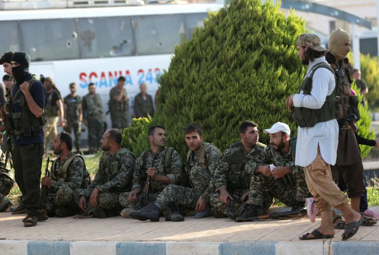 Các tay súng phiến quân HTS đứng gần một nhóm binh sĩ trung thành với Tổng thống Bashar al-Assad được sơ tán khỏi ngôi làng al-Foua và Kefraya.