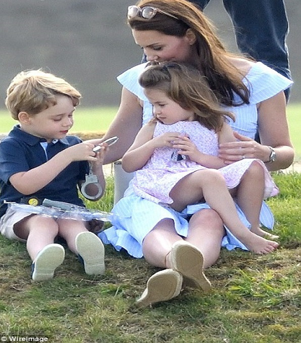 Tiểu Hoàng tử George thích thú nghịch đồ chơi khi ngồi cạnh mẹ, Công nương Kate và em gái Charlotte. Ảnh: WireImage.