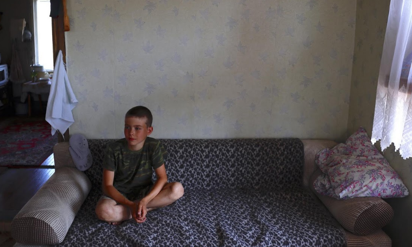 Các bé trai trong ngôi làng này rất yêu thích bóng đá. Ảnh: Jaroslav Aleeksev ngồi xem bóng đá trong nhà bà của cậu.