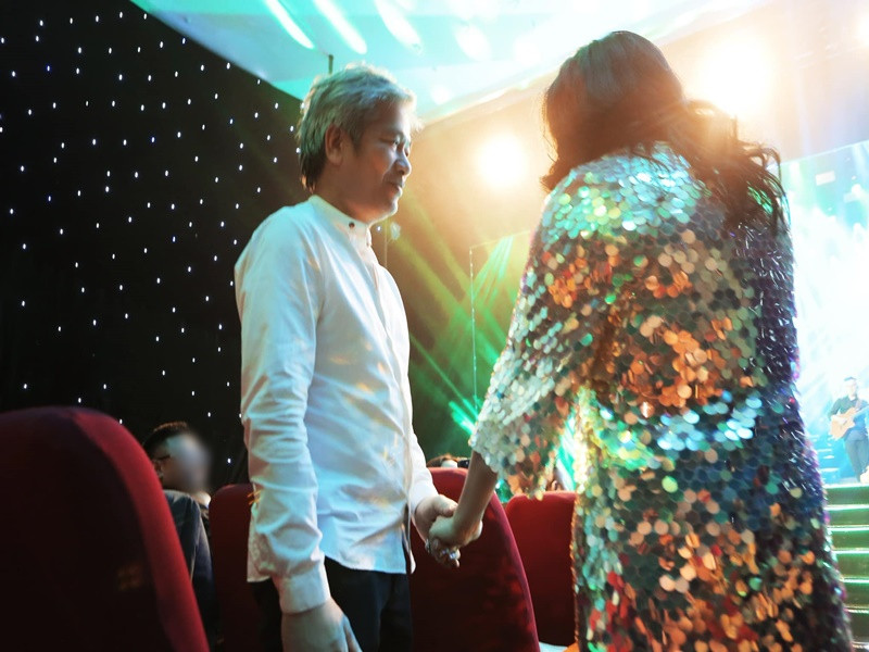 Bác sĩ Tiến Hùng nắm chặt tay Thanh Lam khi cô bước xuống sân khấu trong một buổi biểu diễn.