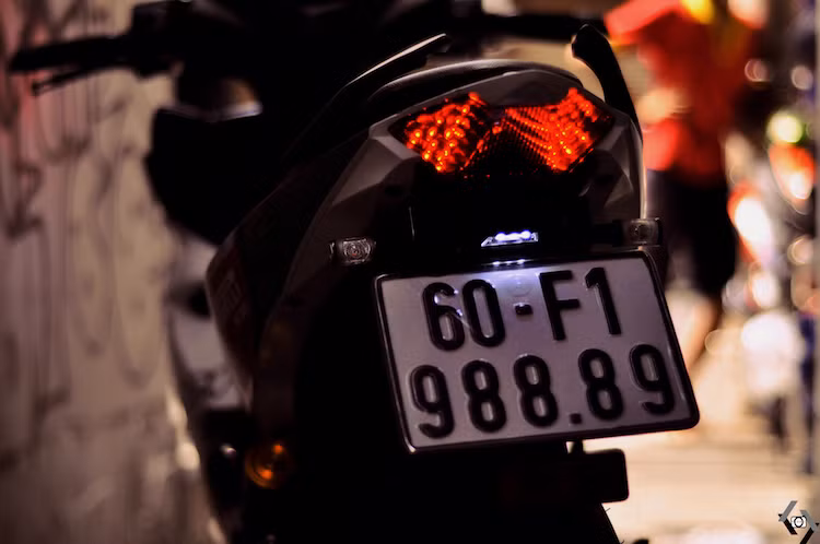 Pát biển số zin khá dài của xe côn tay cỡ nhỏ Yamha Exciter được thay bằng pát rút gọn, kèm theo đèn chiếu sáng biển số và xi-nhan Rizoma.