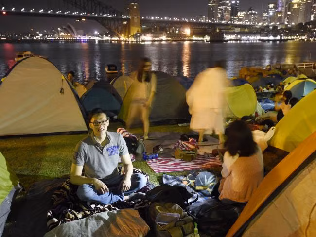 Hai bạn trẻ tên Hank Lee Elaine Zhang (đang cầm di động) cùng đông đảo mọi người còn dựng lều trại ở McMahons Point để canh chỗ đẹp ngắm pháo hoa đêm nay (31/12). Ảnh news.com.au