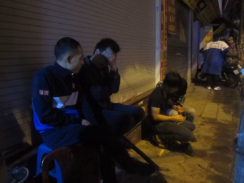 Các phụ huynh trú mưa dưới hiên nhà chờ thay thế xếp hàng.