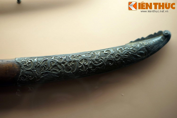 Phần đầu vỏ một thanh gươm lưỡi cong được bọc sắt, chạm trổ hoa lá cầu kỳ. Thanh gươm được trang trí tinh xảo càng đề cao vị thế của chủ nhân.
