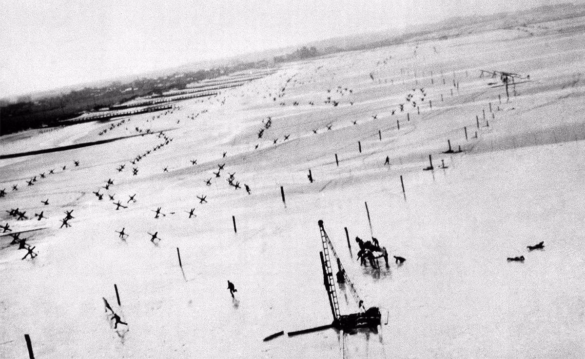 Một chiếc máy bay Đức lượn thấp xuống để chụp ảnh trong khi những binh lính Mỹ đang tấn công lên bãi biển bỏ chạy toán loạn khi thấy máy bay địch lượn sà xuống. Nguồn ảnh: Theatlantíc.