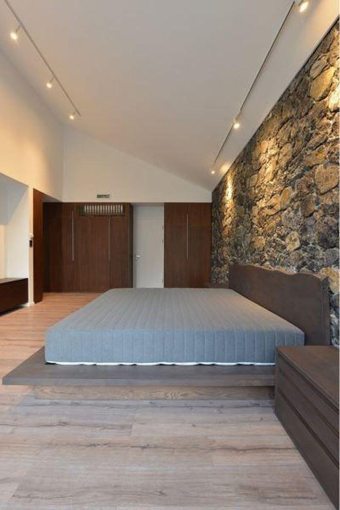 Phòng ngủ thiết kế đơn giản, nổi bật với bức tường đá gần gũi thiên nhiên. Ảnh: Okoncept