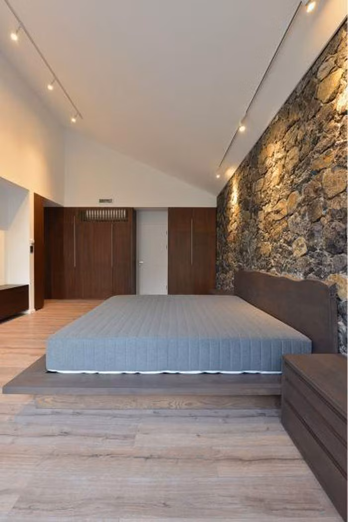 Phòng ngủ thiết kế đơn giản, nổi bật với bức tường đá gần gũi thiên nhiên. Ảnh: Okoncept
